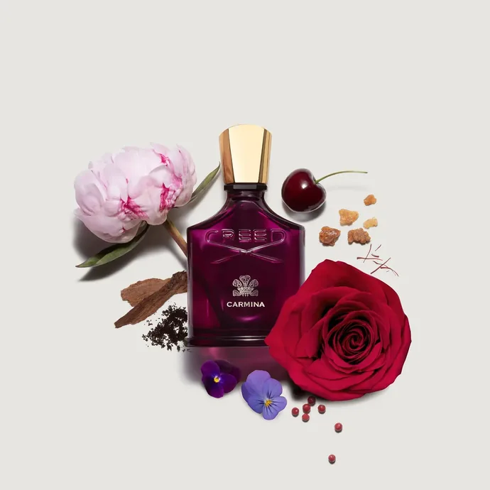 Flacon pourpre Creed Carmina entouré de rose, cerise et éléments floraux